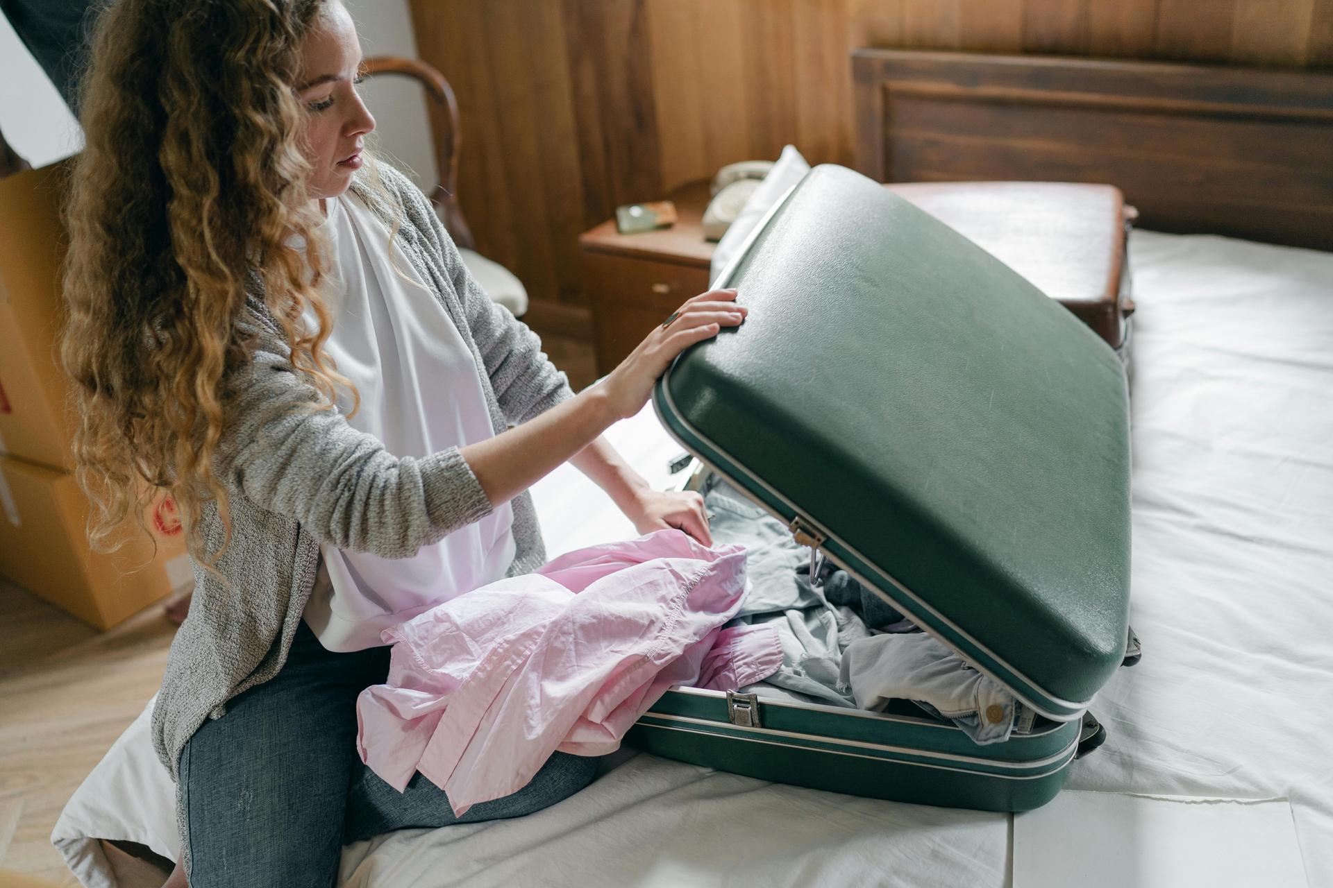 A traveller carefully packs a suitcase on a bed before an international flight home