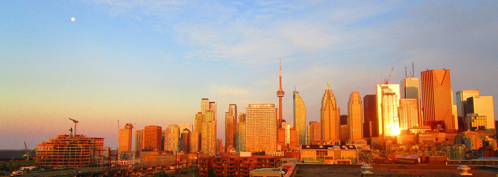 Toronto's downtown skyline at dawn across Lake Ontario, with the CN Tower rising among the office towers.